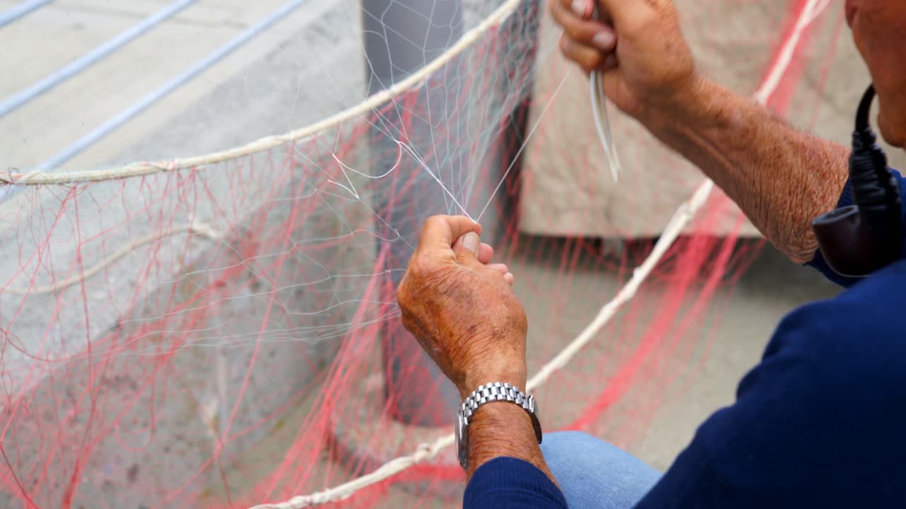 Old fisherman reparing fishing net during the day