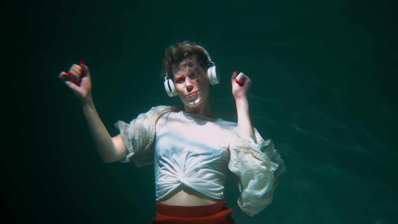 Cinematic under water shot, happy young beautiful woman dancing to music in headphones wearing boho clothes slow motion.