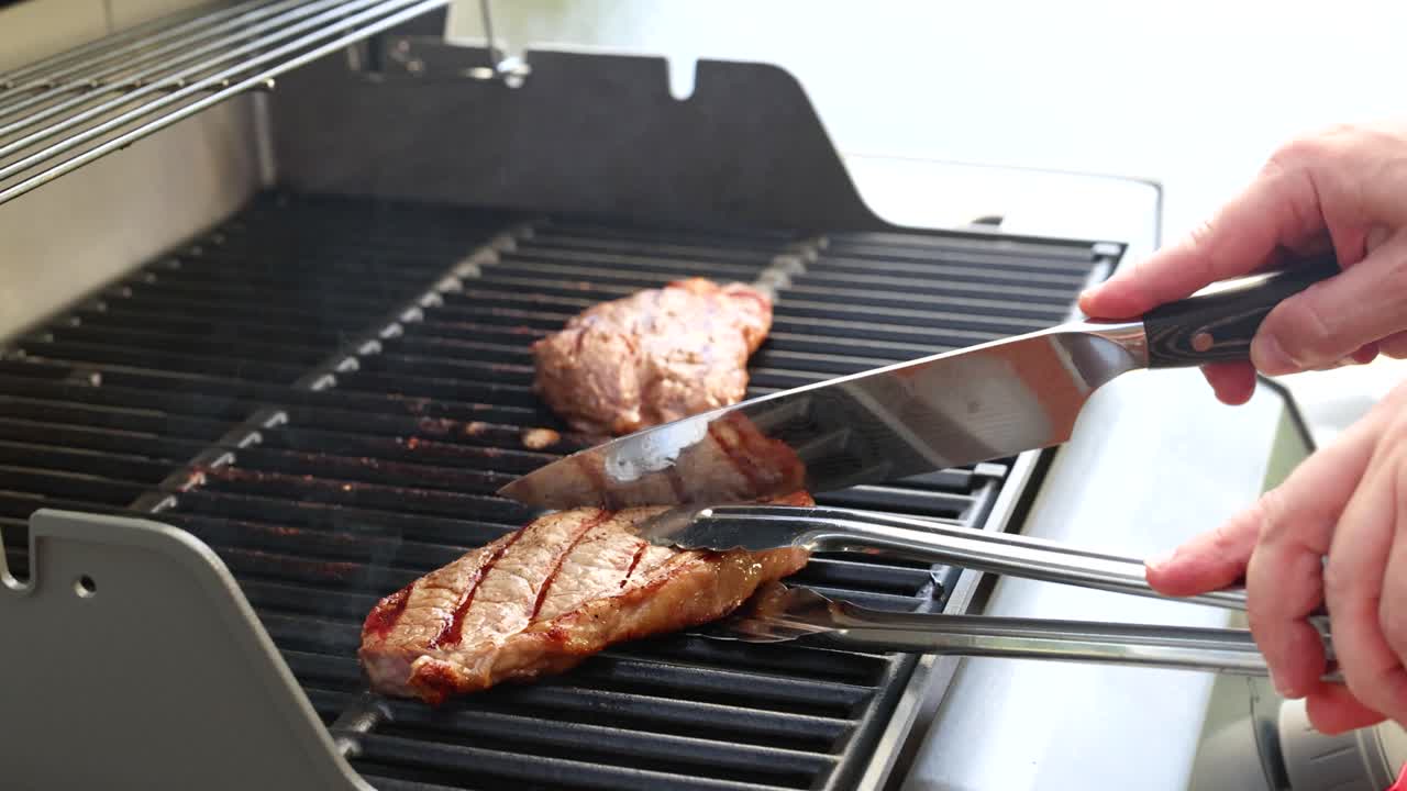 Hands expertly grill beef steak on a barbecue, showcasing cooking techniques. Bright outdoor lighting enhances the sizzling process