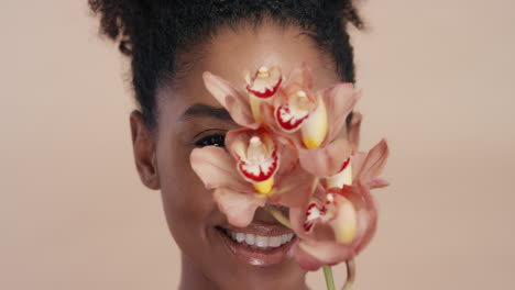 retrato de belleza hermosa mujer afroamericana posando juguetonamente con una flor de orquídea tocando una piel sana disfrutando de la suave fragancia de la esencia natural concepto de cuidado de la piel