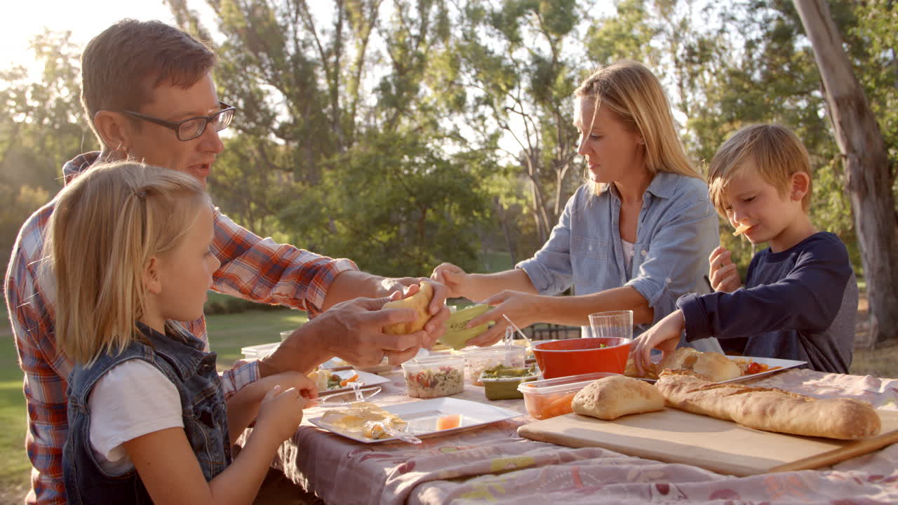 una joven familia blanca disfrutando de un picnic en una mesa en un parque