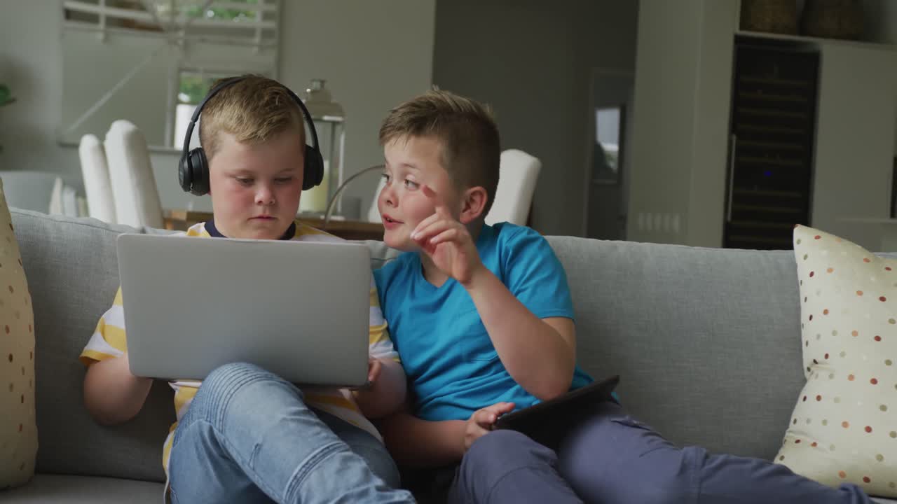 niño caucásico con su hermano sentado en la sala de estar y usando una computadora portátil
