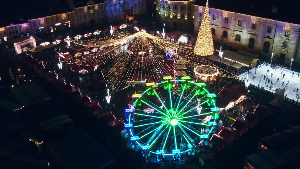 Aerial drone view of The Big Square in Sibiu at night, Romania. Old city centre decorated for Christmas. Ferris wheel, skating rink, people