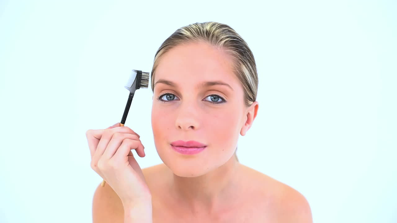 una mujer atractiva cepillándose las cejas.