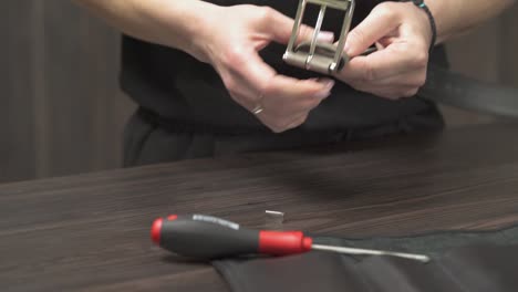 a close-up of female shop assistant attaching the buckle to the black leather belt using special tools. shop and sale concept.