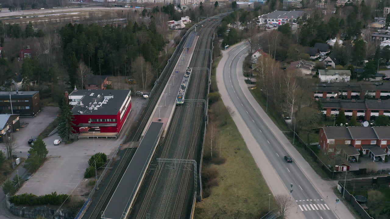 A drone passes over the train tracks and roads in a Scandinavian city tilting down from the orange skyline to the grey pathways of trains and cars
