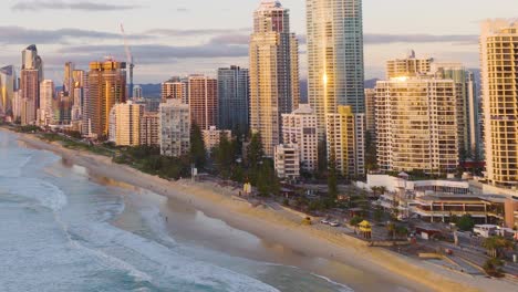 aerial footage of gold coast's beachfront skyline during sunset, highlighting tall buildings, sandy beaches, and ocean waves