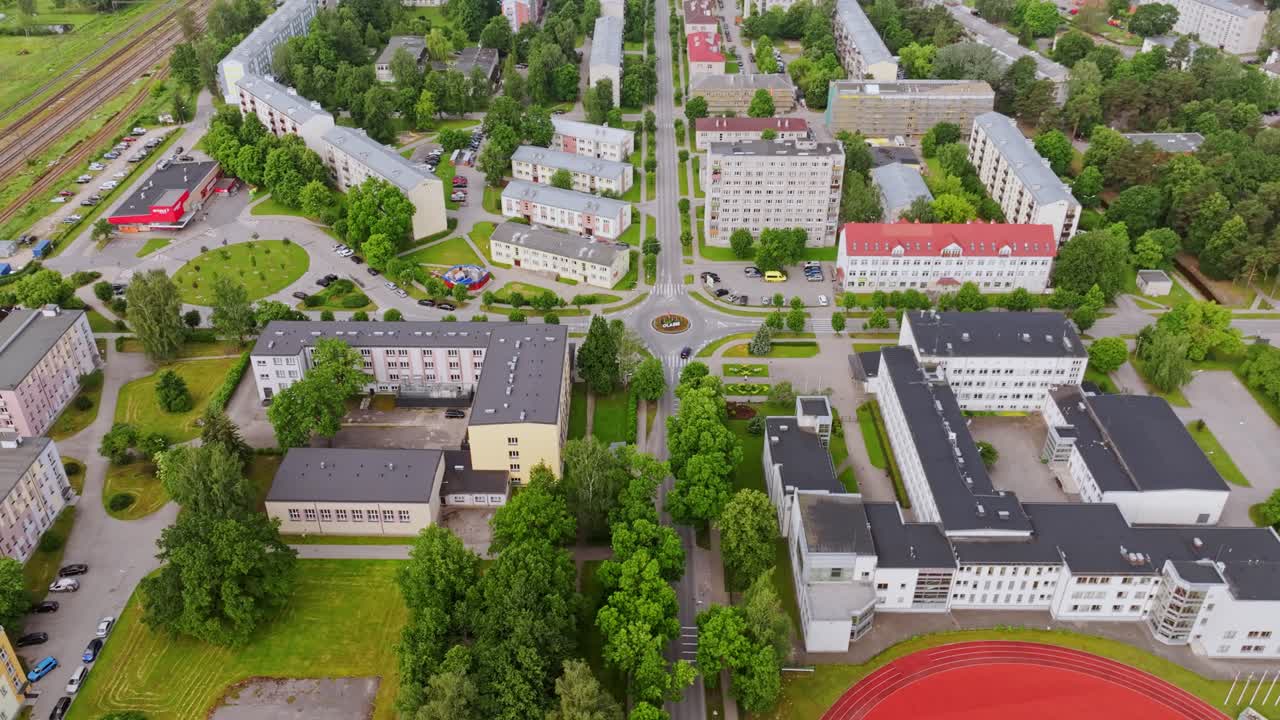Drone tilting up and away over urban district with school building and stadium