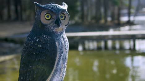 a plastic owl keeping watch over a lake on a deck