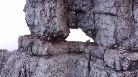 epic fpv drone aerial flying through hole in steep rocky stone formation on mountain top in alpine mountains