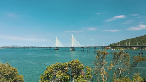 drone aerial side view of concrete cable-stayed bridge road above turquoise color tropical ocean, located in laguna, santa catarina, brazil