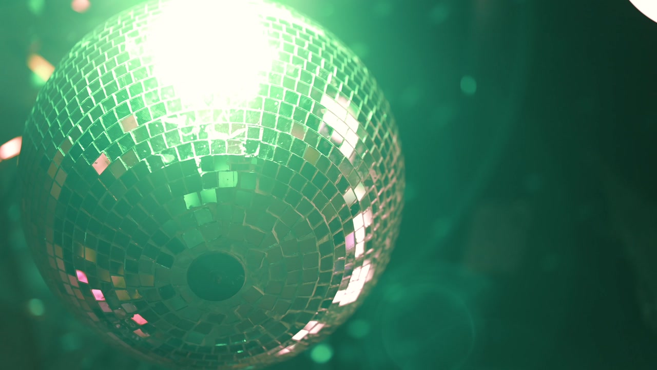 Close-up of a disco mirror ball reflecting green light in a dark party atmosphere.