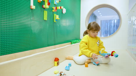 little girl child plays lego color constructor sitting on floor at inside playroom - slow motion