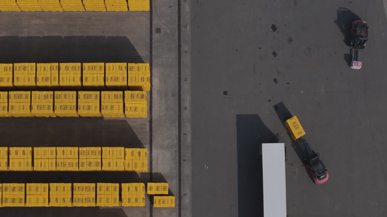 Forklift operating in logistics yard in Po Valley Emilia Romagna Italy handling stacked construction blocks near truck trailer within industrial storage area, drone top down shot