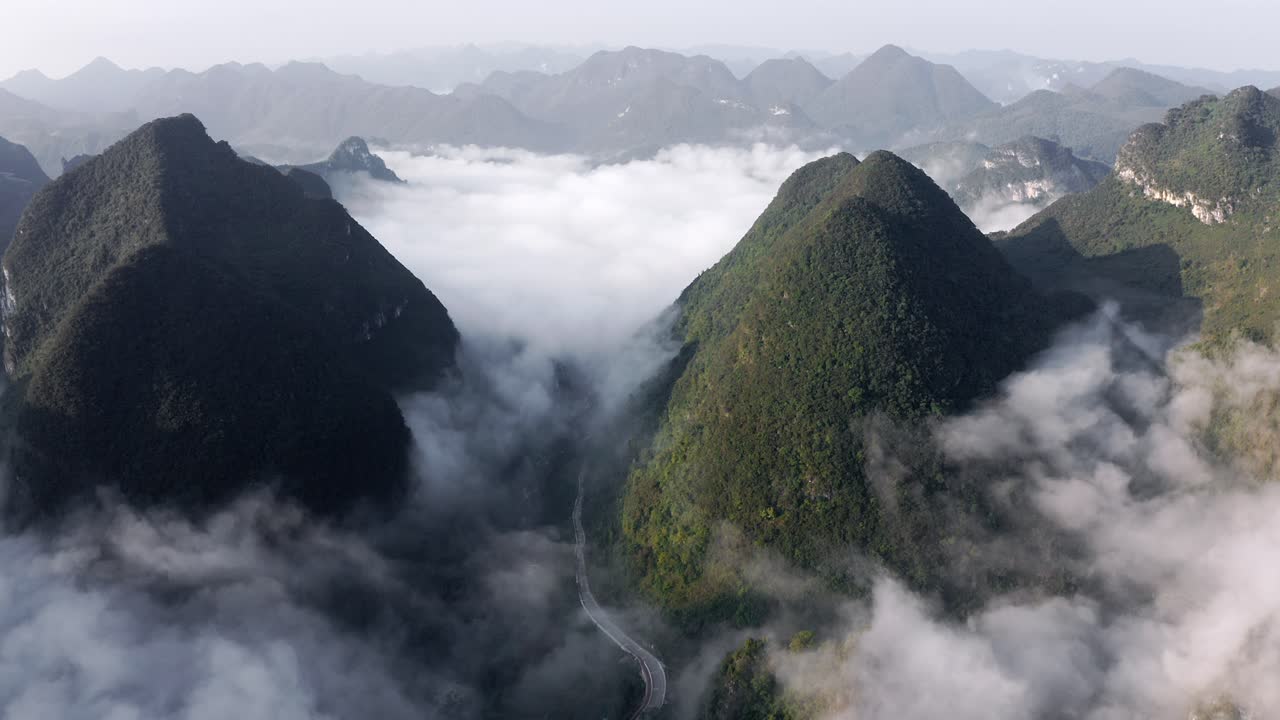 montañas kársticas asiáticas que se elevan por encima de las nubes y un pequeño pueblo chino, antena