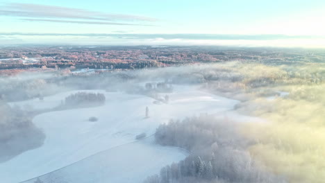 Toma-Aérea-De-Ensueño-Volando-Sobre-El-Hermoso-Paisaje-Invernal-De-Un-Pueblo-Cubierto-De-Nieve-Y-Una-Capa-De-Niebla