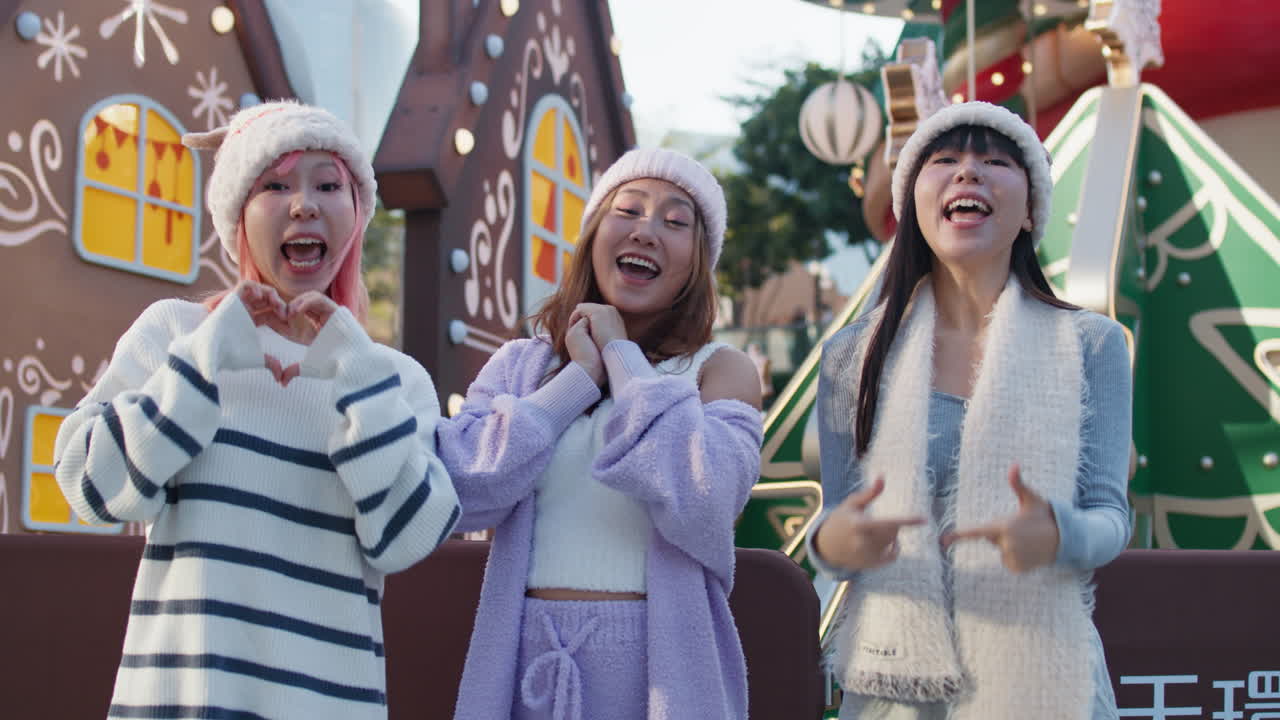Three young women pose in front of a gingerbread house during the holidays