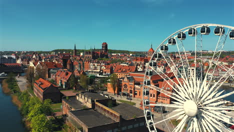 Drones-Volando-Alrededor-De-La-Noria-En-Gdańsk-Con-El-Casco-Antiguo-Y-Las-Viviendas-Al-Fondo-En-Un-Día-Soleado-De-Verano