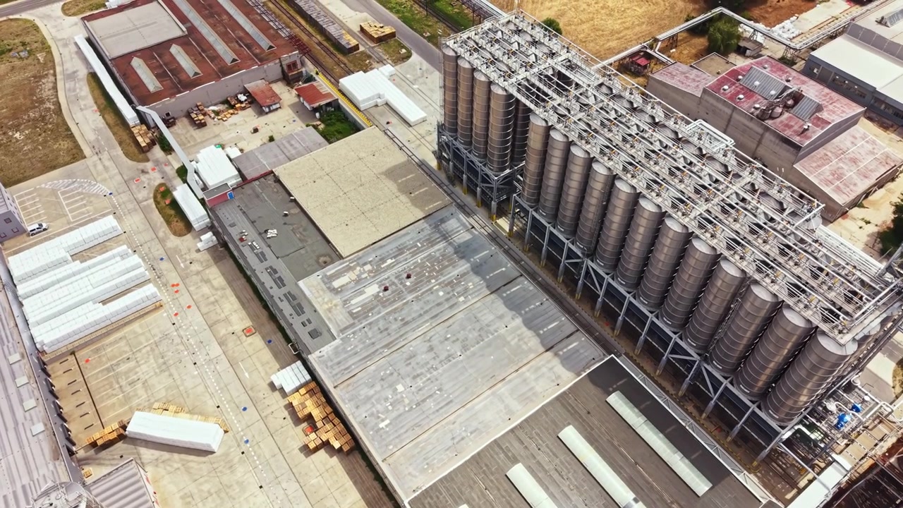 Grande instalação industrial com silos e áreas de produção vista de cima durante o dia.