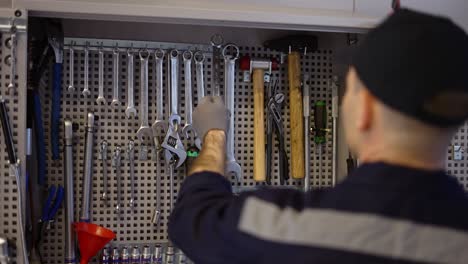 a car mechanic stands near the stand with wrenches, take the required size, slow motion