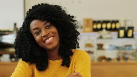 close-up view of african american woman with curly hair smiling at camera sitting at a table in a cafe