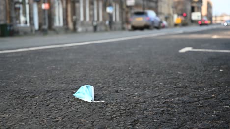 Gebrauchte-Gesichtsmaske,-Die-An-Einem-Sonnigen-Tag-Am-Straßenrand-Im-Vollen-Verkehr-Weggeworfen-Wird