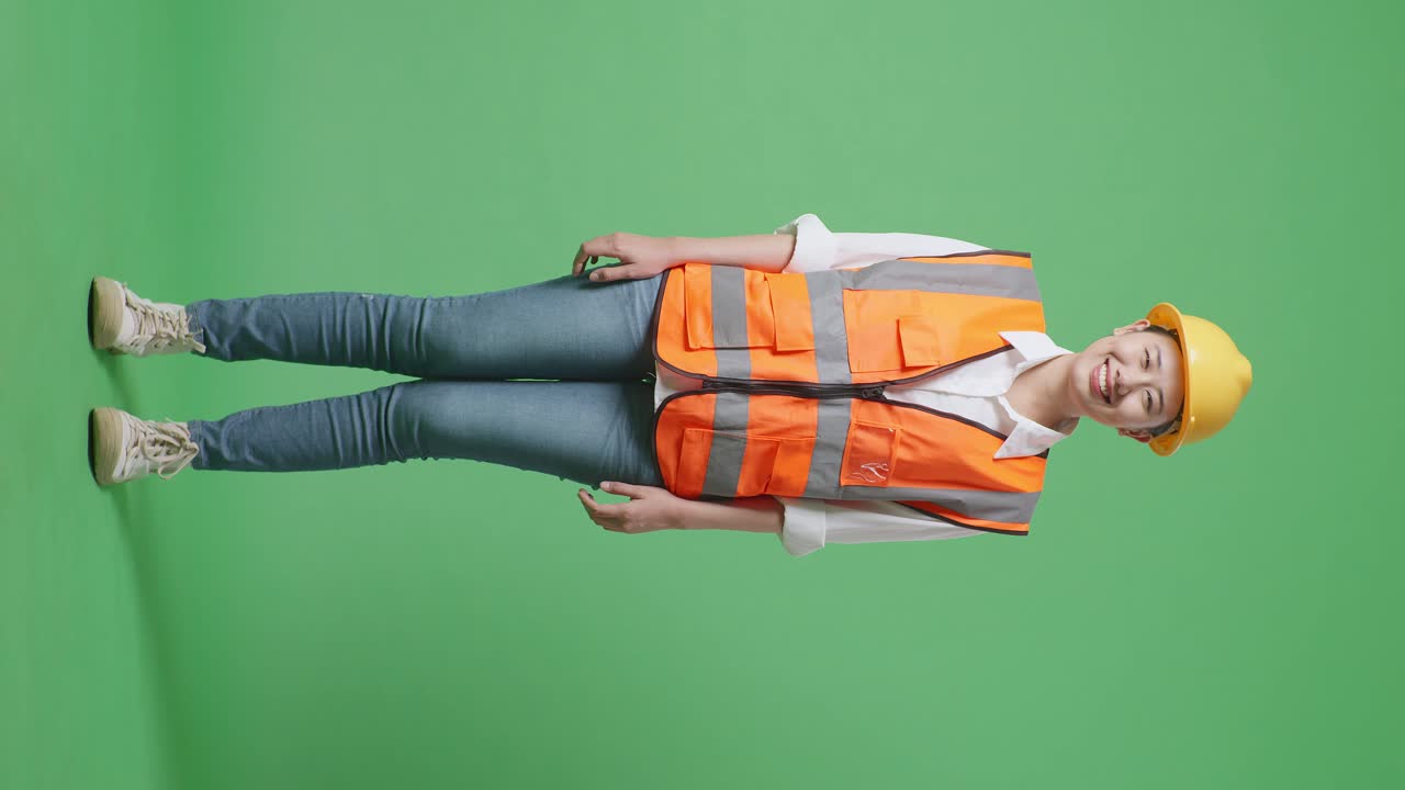 안전 헬을 입은 아시아 여성 엔지니어의 몸 전체가 녹색 스크린 배경 스튜디오에 서서 카메라에 미소 짓고 있습니다.