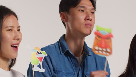 side view of group of young friends in front of white studio background having fun posing for photo booth style portraits with props 3