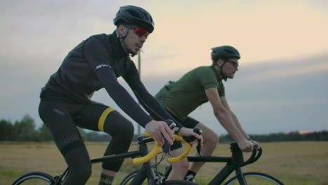 Dos-Ciclistas-Viajan-Por-La-Carretera-Por-La-Noche-Después-Del-Atardecer.-Temprano-En-La-Mañana-Entrenando-A-Ciclistas-Con-Cascos.