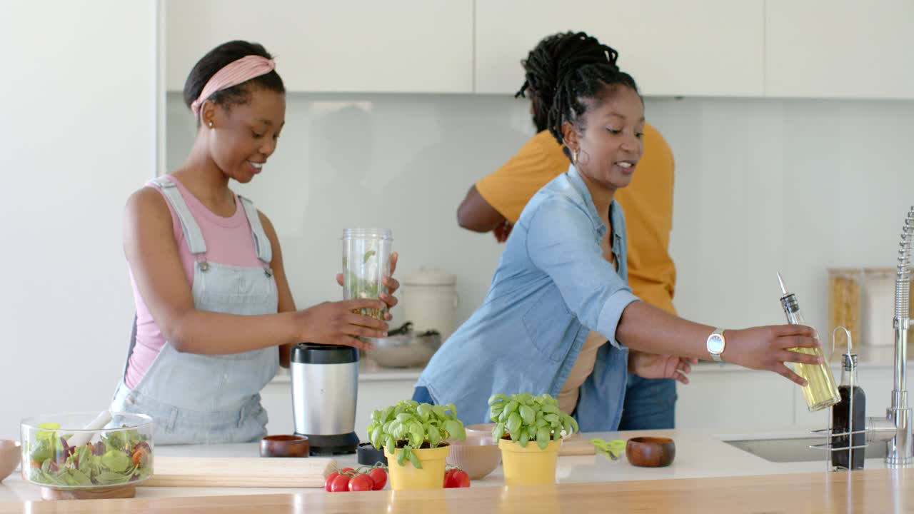 Mamma e adolescente afroamericani versano olio nel frullatore, fissano il coperchio, preparano un condimento in cucina