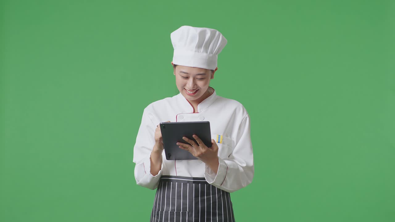 Asian Woman Chef Taking Note On A Tablet While Standing In The Green Screen Background Studio