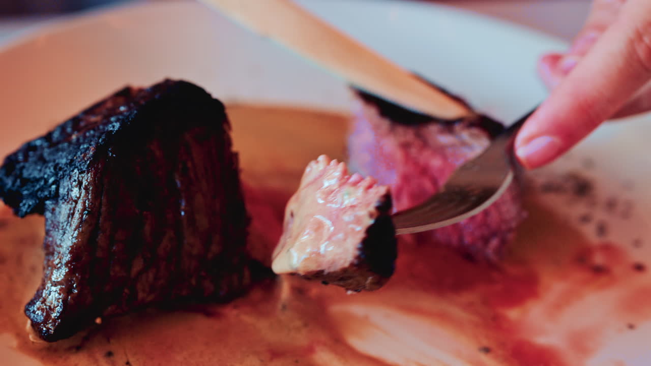 Close up of a knife slicing through a medium rare steak, exposing its tender, juicy interior