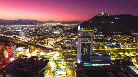 Aerial-Hyperlapse-Drone-Fly-Above-Baquedano-Santiago-Chile-at-Sunset-Nighttime-Street-Network-of-Latin-American-Vibrant-Capital,-Andean-Cordillera-Pink-Background