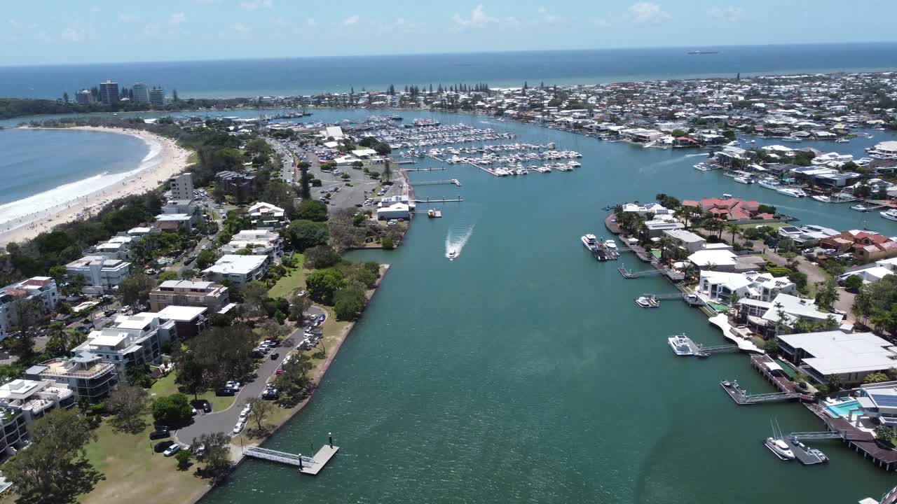 Aerial view of a harbour flying over high rise apartments and towards a sandy beach in Australia