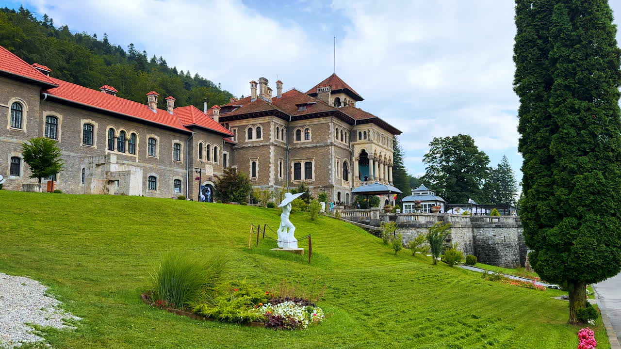 Busteni, Romania, 17 July 2025: Walking by the green lawn with a beautiful statue in front of the historical building. Exterior of Cantacuzino Castle in Busteni, Romania
