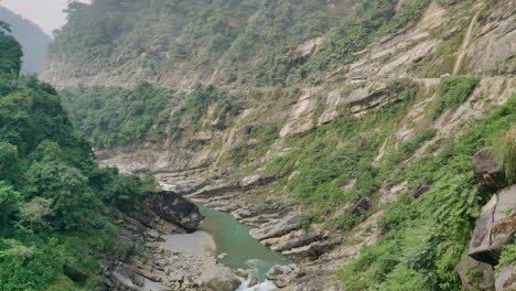 vehicles passing on a dangerous dirt road with mountains on one side and river on the other side