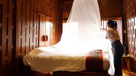 person arranging mosquito net over bed in wooden room