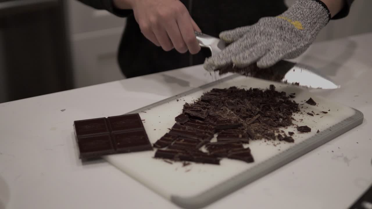 una niña corta chocolate negro antes de derretirlo para hacer galletas de mantequilla millonarias mientras usa guantes de seguridad