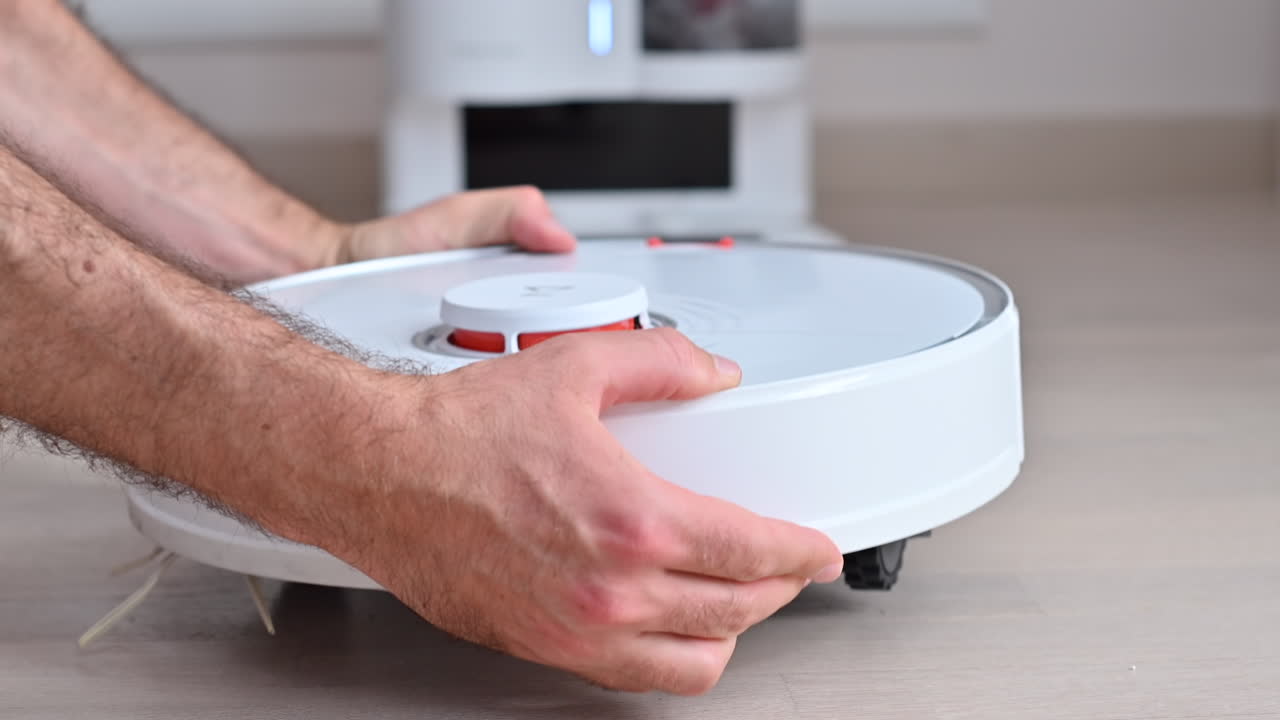 Mężczyzna naprawia biały robot odkurzający