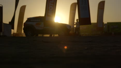 silhouette of racing car and truck driving in slow motion on a sunset at dakar rally camp