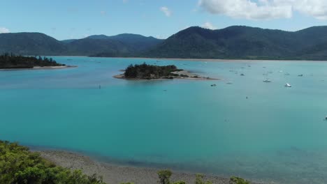 Vista-Aérea-Hacia-Adelante-Sobre-La-Isla-Whitsundays-En-Australia-Con-Yates-Amarrados-Y-Montañas-En-Segundo-Plano