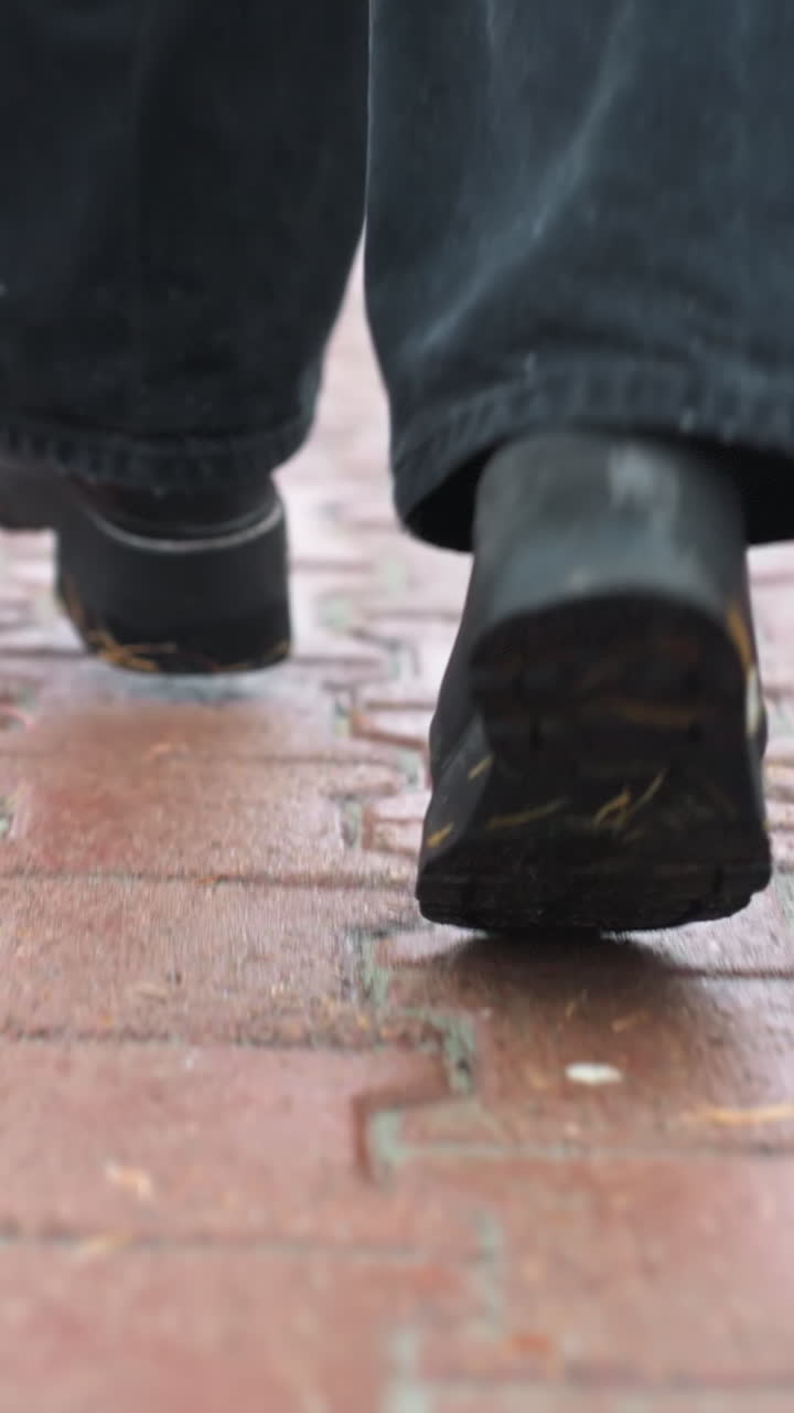 Back shot of person's legs running during light snowfall wearing black jeans and black boots, autumn leaves scattered across path, creating peaceful winter atmosphere with light breeze