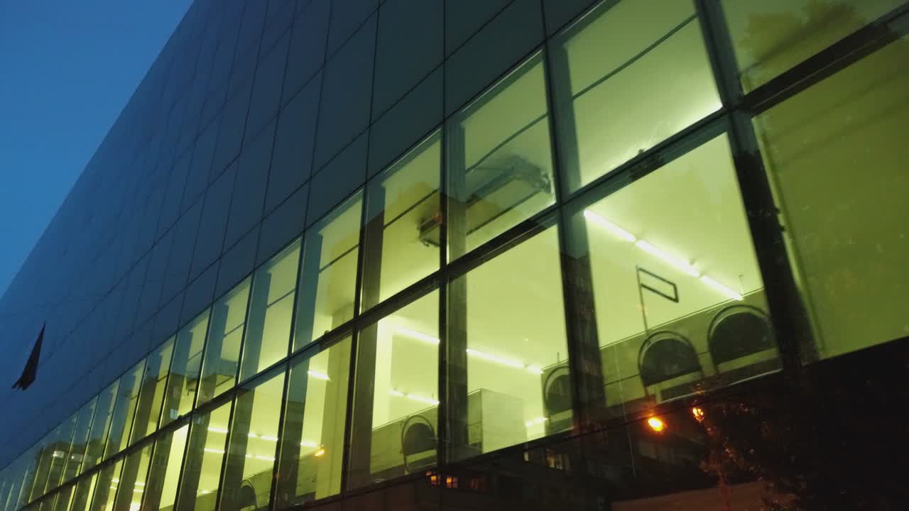 vista exterior de 4k del edificio del distrito comercial, centro comercial con ventanas de espejo de pared por la noche o por la noche. reflejo de la ciudad, la gente, los coches en las paredes espejadas. cámara de dron moviéndose. personas que trabajan dentro