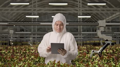 asian man researcher using tablet while standing in the greenhouse with smart robotic farmers