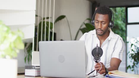 Happy-african-american-man-sitting-at-table-in-kitchen,-using-laptop-and-making-vlog