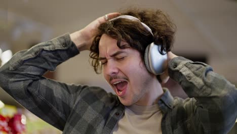 Close-up-of-a-happy-brunette-guy-with-curly-hair-listens-to-music-loudly-on-his-wireless-headphones-and-sings-while-shopping-in-a-supermarket