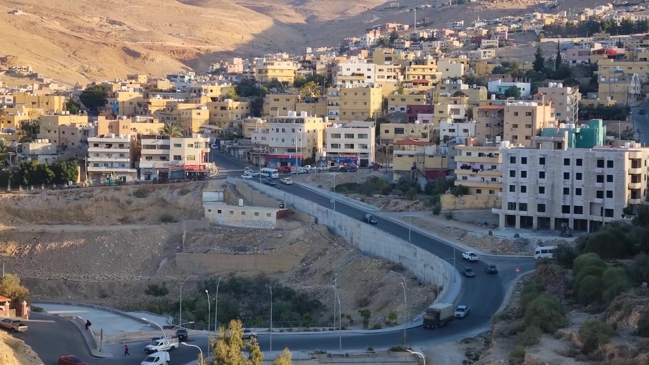 Il traffico mattutino scorre attraverso Wadi Musa, Giordania, mentre l'alba illumina il quartiere collinare e le strade della valle. Uno scorcio pacifico della vita quotidiana vicino all'antica città di Petra