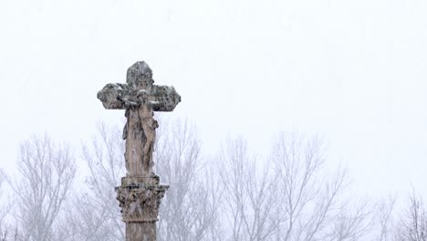 christian cross on top of a stone pillar under a winter snowstorm