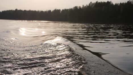 big wave on a lake while in a boat with sun shining in the background blurry forest moody evening atmoshere