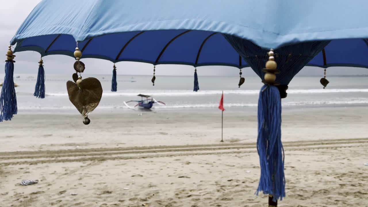 Tropical island charm at Bali’s Kuta Beach where colorful umbrellas frame the sandy shoreline and a jukung boat rests against the gentle surf offering travelers a coastal view of paradise